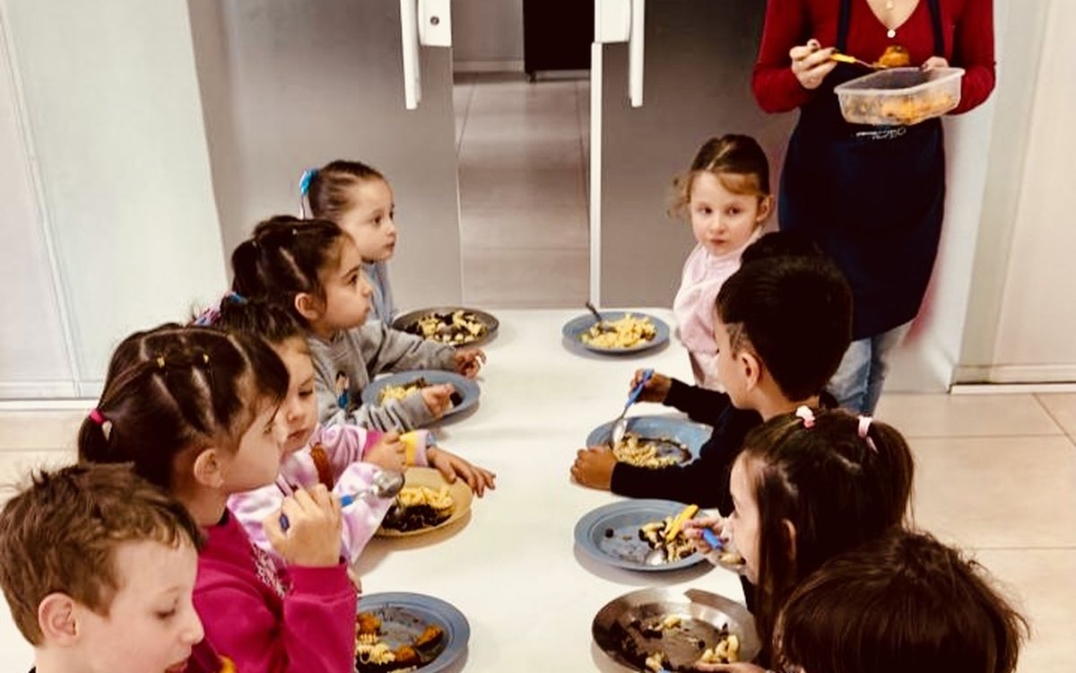 Turma almoçando à mesa com a professora servindo
